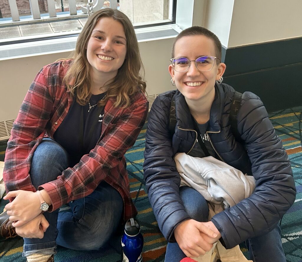 Two women sitting on the floor and smiling.