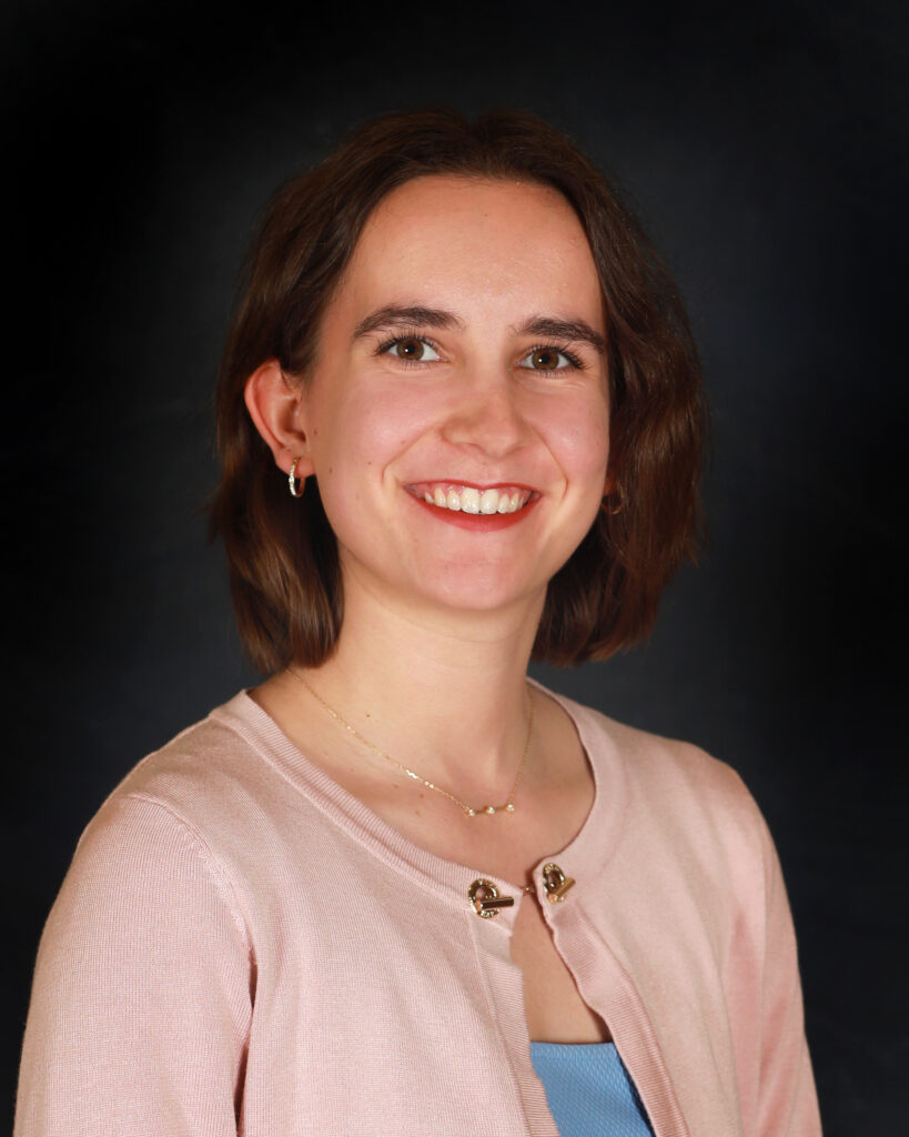 Professional headshot of a young woman wearing a light blue dress and pale pink cardigan.