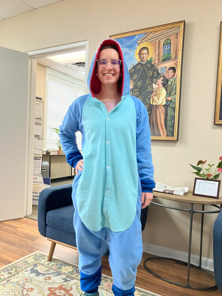 A woman smiling and wearing a blue onesie themed to look like Stitch from the Lilo and Stitch movies