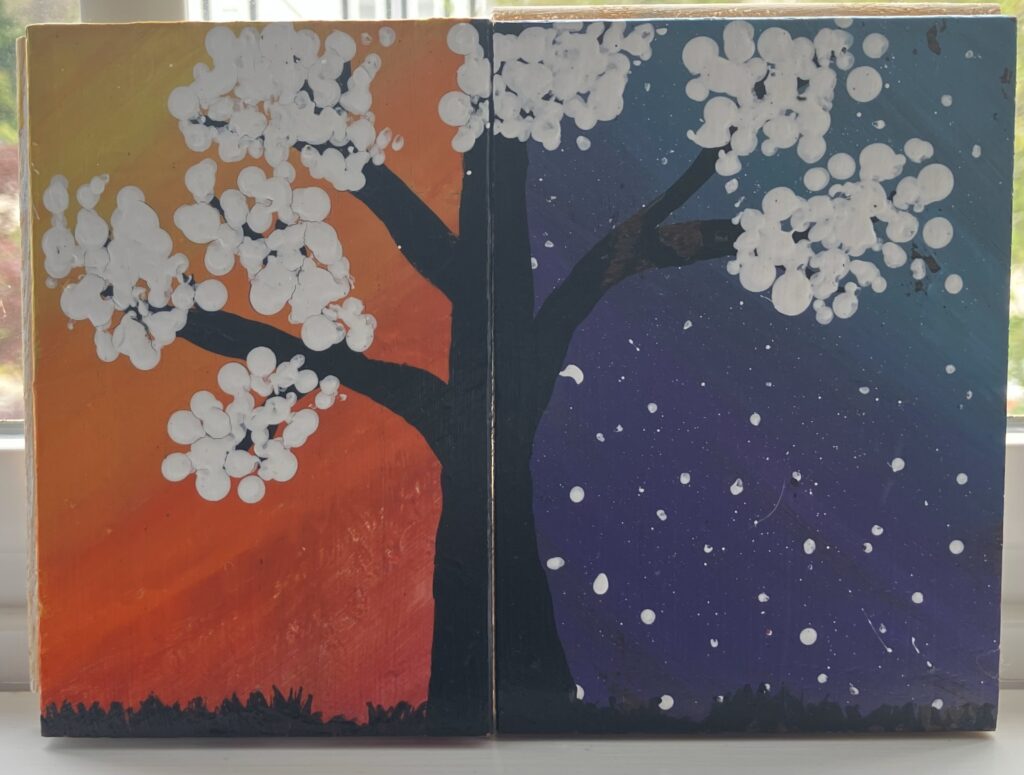 Acrylic painting of a black tree with white flowers. The tree is split in half between two pieces of wood; the left side is in front of a yellow, orange, and red sunrise; the right side is in front of a dark purple and blue night sky with white stars.