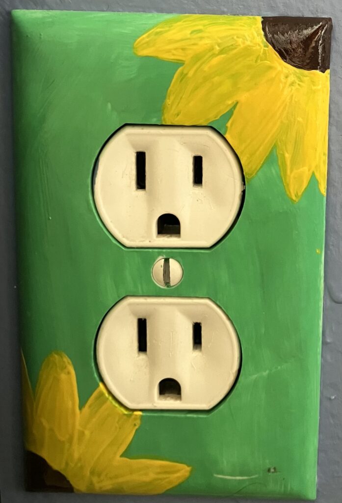 Acrylic paint on a plastic outlet covering. The background is light green with two yellow sunflowers in the top right corner and bottom left corner.
