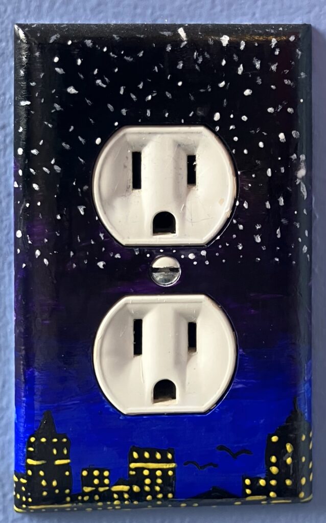 Acrylic paint on a plastic outlet cover. The design is a city skyline at night; there are black apartment buildings with yellow lights on in the windows; there is the outline of two birds flying close to the tops of the apartments, toward the top, there are stars in the sky.