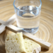 A wooden plate with a cup of water, a piece of bread, and a wooden cross on it.