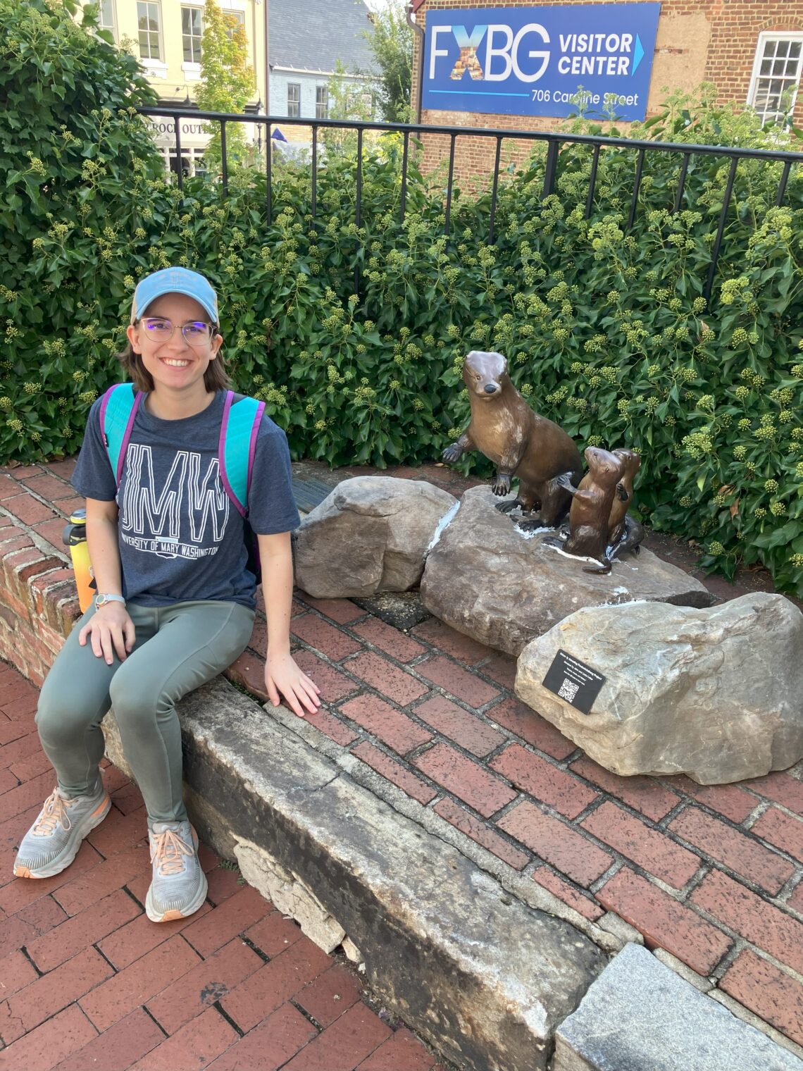 A young woman sitting next to a statue of a mother otter and her two pups.