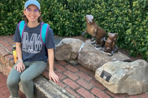 A young woman sitting next to a statue of a mother otter and her two pups.