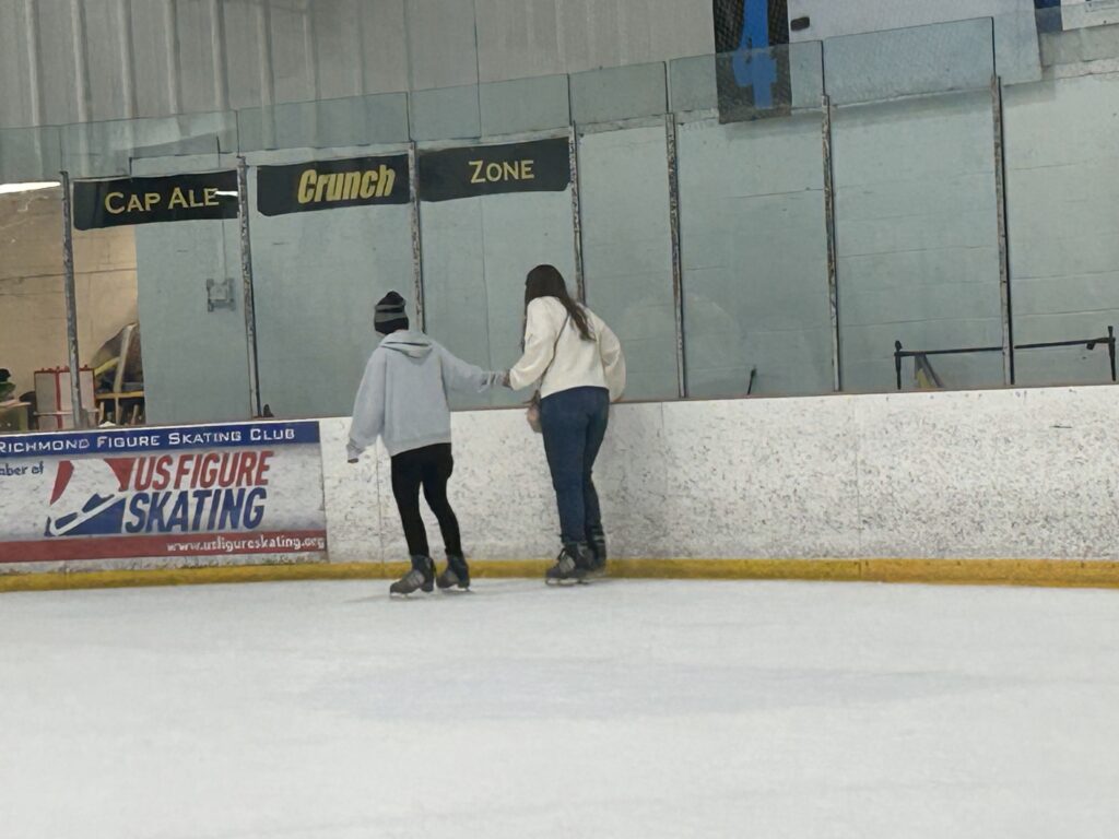 The backs of two women as they ice skate and hold hands for balance.
