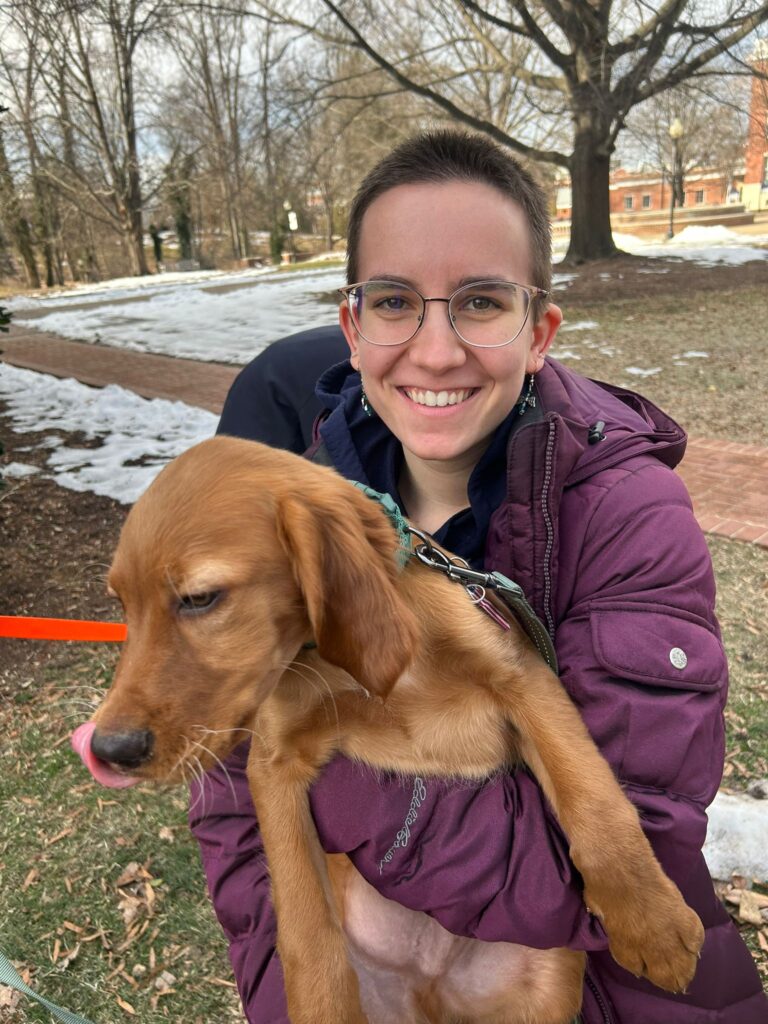 A woman smiling while holding a puppy who's trying to escape her arms.