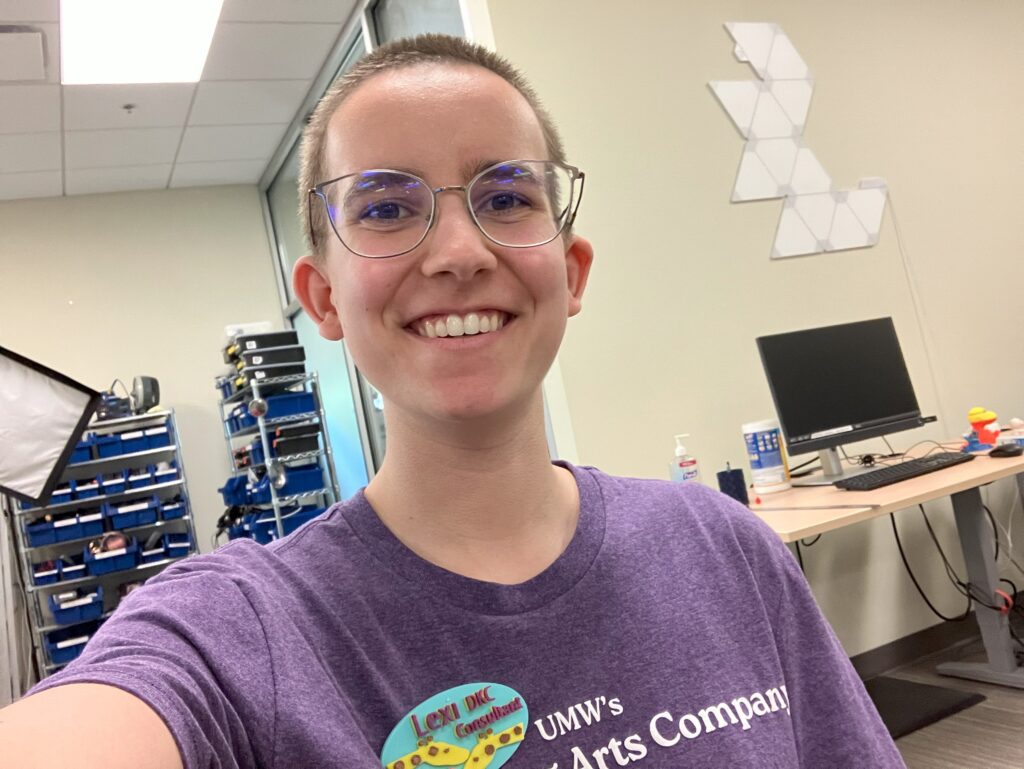 A selfie of a smiling woman wearing a 3D-printed nametag with a giraffe design and the words "Lexi, DKC Consultant"