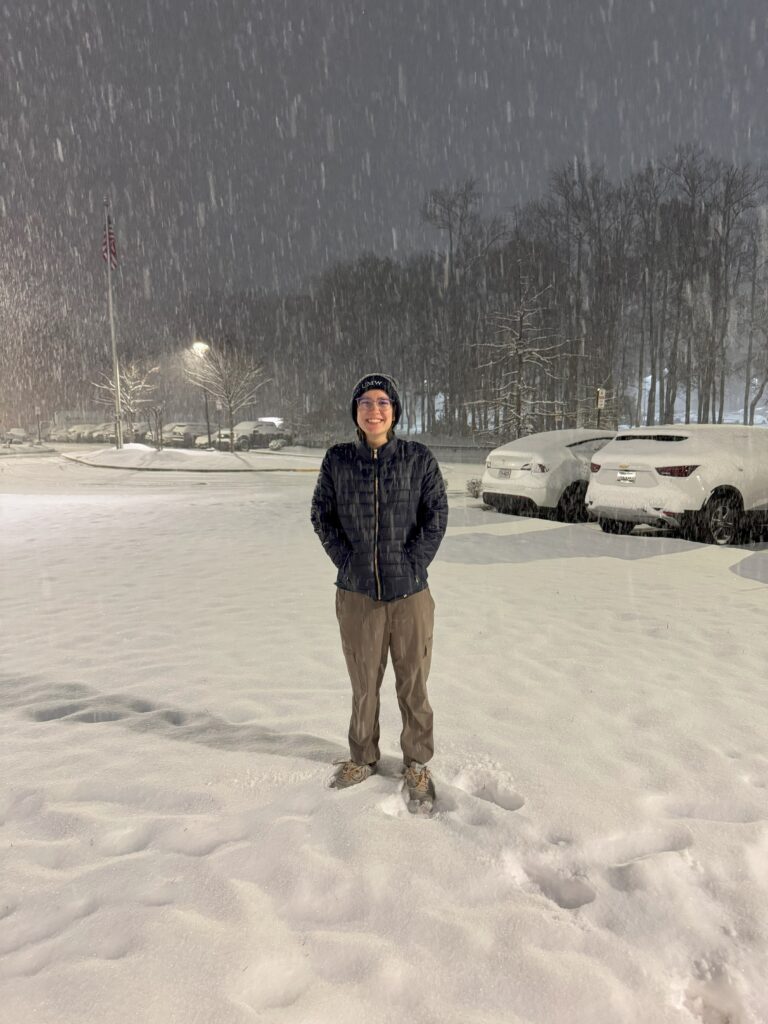 A woman standing and smiling in a snowy parking lot.