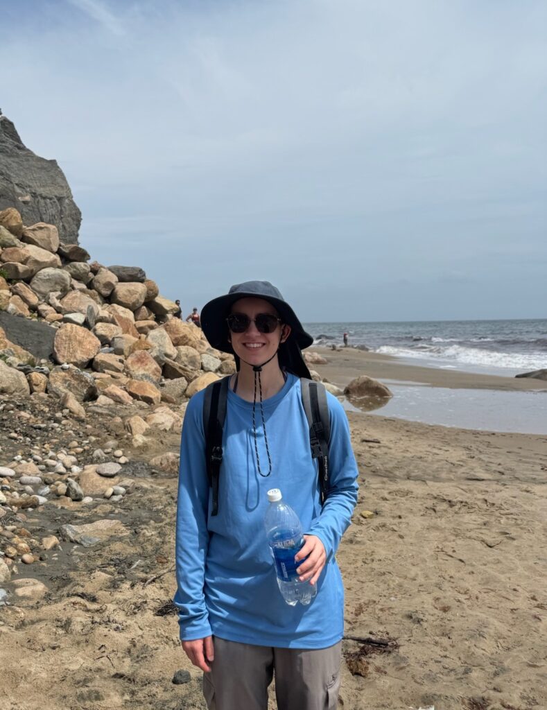 Me standing on a beach in front of a rocky cliffside.