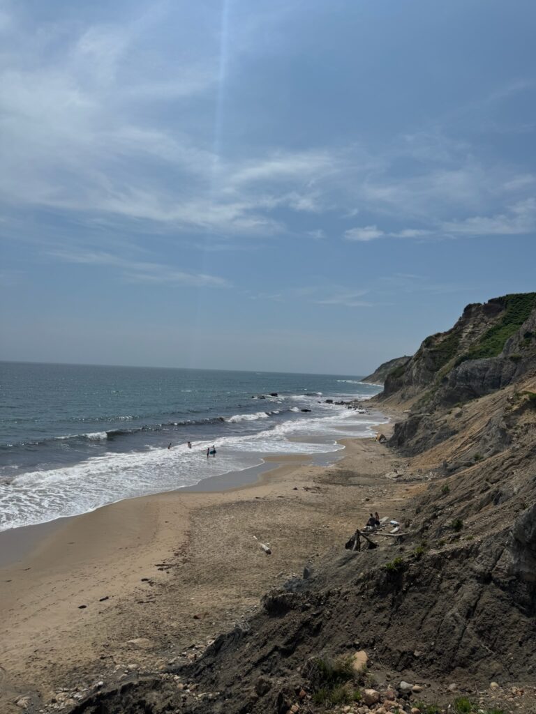 A cliffside leading to a sandy beach with a blue sky above.