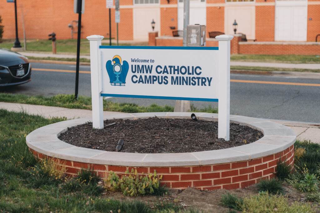 A sign in the lawn scaping reading, "Welcome to UMW Catholic Campus Ministry."