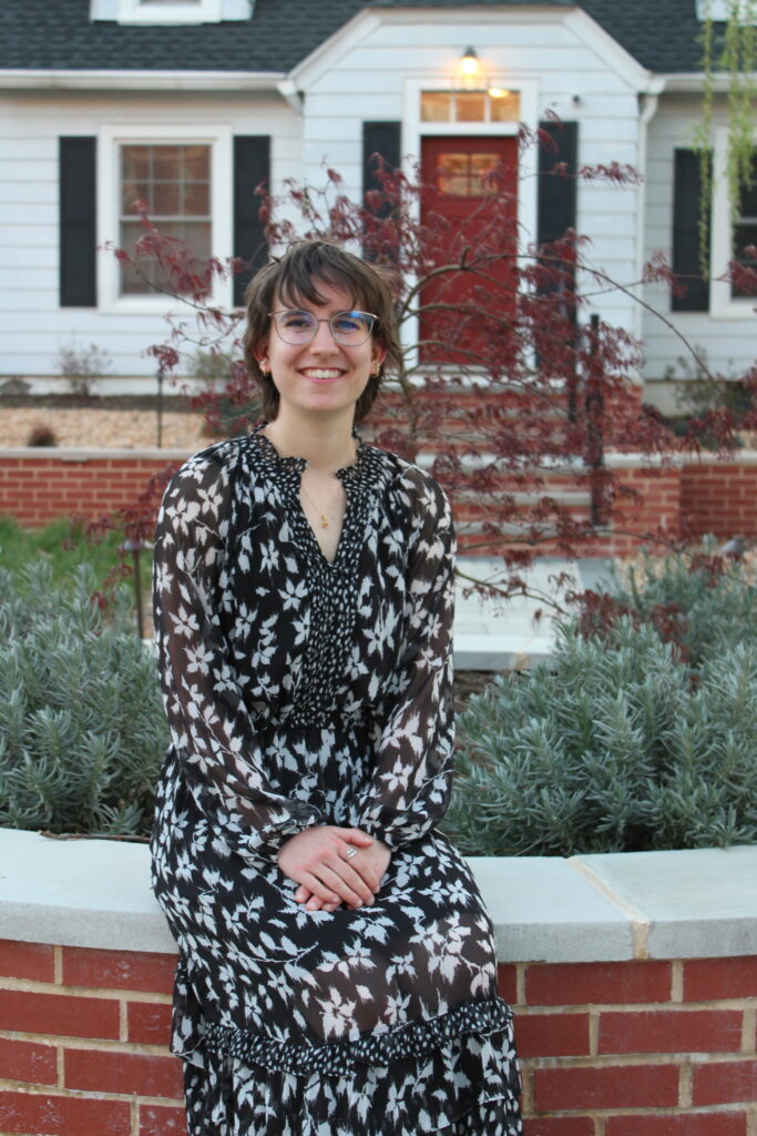 Lexi smiling and posing sitting down, wearing a black and white dress.
